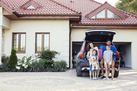 Happy family standing in front of car packed for vacation stock photo