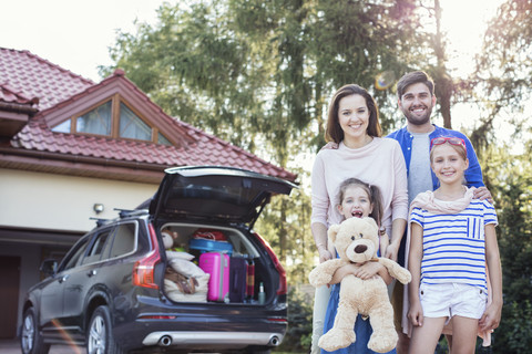 Happy family standing in front of car packed for vacation stock photo