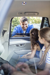 Father standing at car window, talking to his daughters sitting in back seat - WEST22314