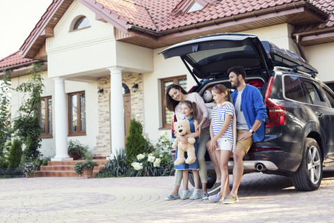Glückliche Familie vor einem für den Urlaub gepackten Auto, lizenzfreies Stockfoto