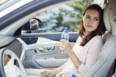 Frau sitzt im Auto und hält eine Flasche Wasser - WEST22333