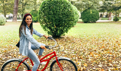 Lächelnde junge Frau auf dem Fahrrad in einem Park - MGOF02696