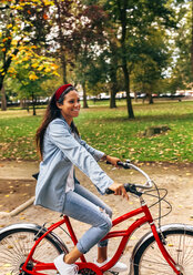 Lächelnde junge Frau auf dem Fahrrad in einem Park - MGOF02697