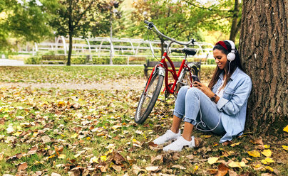 Young woman listening to music with her smartphone in a park in autumn - MGOF02704