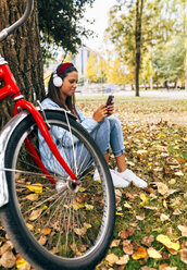 Junge Frau hört Musik mit ihrem Smartphone in einem Park im Herbst - MGOF02705