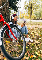 Young woman listening to music with her smartphone in a park in autumn - MGOF02705