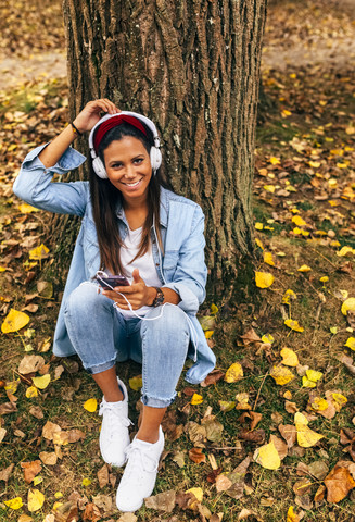 Junge Frau hört Musik mit ihrem Smartphone in einem Park im Herbst, lizenzfreies Stockfoto