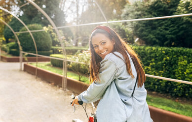 Lächelnde junge Frau auf dem Fahrrad in einem Park - MGOF02711