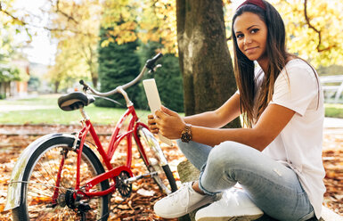 Portrait of smiling young woman in a park in autumn holding a tablet - MGOF02712