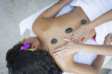 Young woman receiving a massage with heated stones on her back - ABAF02104