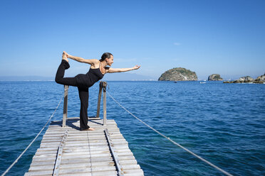Woman practicing yoga on small dock at the cean - ABAF02118