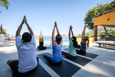 Yoga group with teacher exercising at ocean front villa - ABAF02120