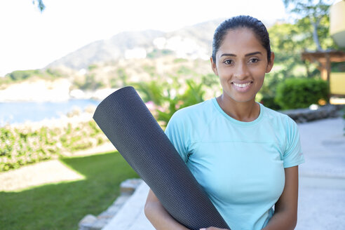 Portrait of smiling woman holding rolled up yoga mat - ABAF02123