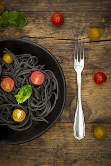 Schüssel mit Spaghetti al Nero di Seppia mit Tomaten und Gabel auf Holz - LVF05726