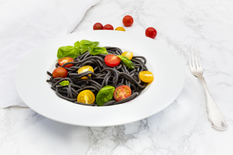 Teller mit Spaghetti al Nero di Seppia mit Tomaten und Basilikumblättern, lizenzfreies Stockfoto