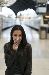 Happy young woman with cell phone at train station - KKAF00188