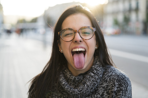 Portrait of happy young woman with glasses sticking her tongue out stock photo