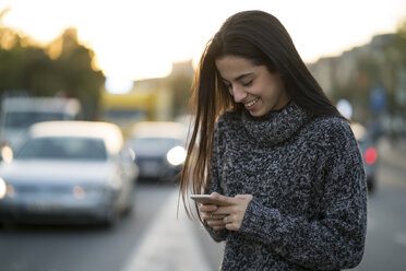 Lächelnde junge Frau, die auf der Straße ein Mobiltelefon benutzt - KKAF00199