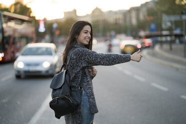 Smiling young woman hitchhiking on urban street - KKAF00201