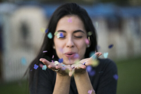 Happy young woman blowing confetti outdoors - KKAF00206