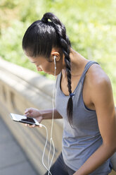 Female athlete listening to music with smartphone - GIOF01698