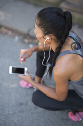 Female athlete listening to music with smartphone - GIOF01701