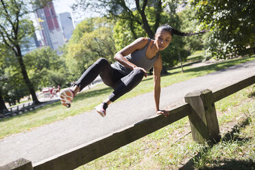 Woman jumping over fence in park - GIOF01716