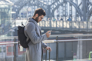 Geschäftsmann mit Gepäck schaut auf Handy am Bahnhof - TCF05236