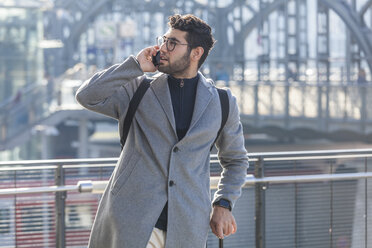 Businessman with baggage on the phone at train station - TCF05237