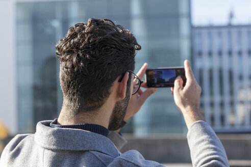 Rückansicht eines Mannes, der ein Foto mit seinem Smartphone macht - TCF05241