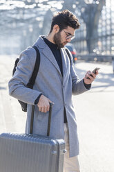 Geschäftsmann mit Gepäck schaut auf sein Handy - TCF05243