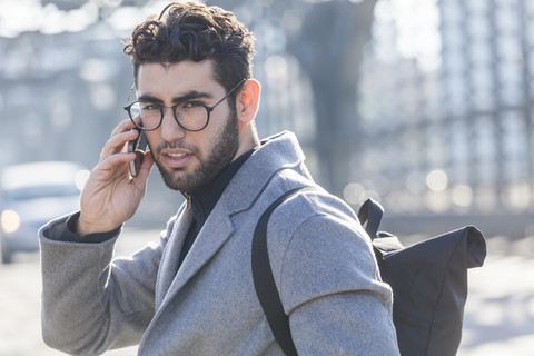 Porträt eines jungen Geschäftsmannes mit Rucksack, der telefoniert, lizenzfreies Stockfoto