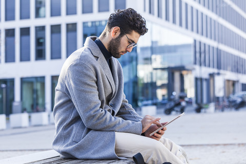 Young man sitting on bench using mini tablet stock photo