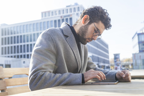Junger Mann sitzt auf einer Bank und benutzt ein Mini-Tablet, lizenzfreies Stockfoto