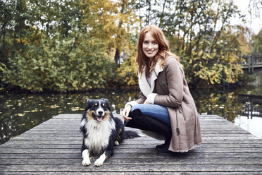 Porträt einer lächelnden Frau mit ihrem Hund auf einem Bootssteg im Herbst - SRYF00143