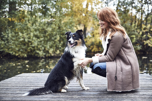 Smiling woman with her dog on jetty in autumn - SRYF00144