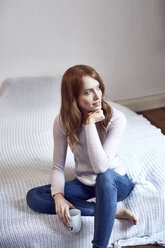 Portrait of redheaded woman sitting on bed with cup - SRYF00145