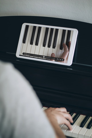 Man learning playing piano with video tutorial on a tablet stock photo