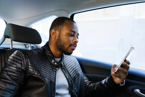 Junger Mann benutzt Smartphone im Taxi, lizenzfreies Stockfoto