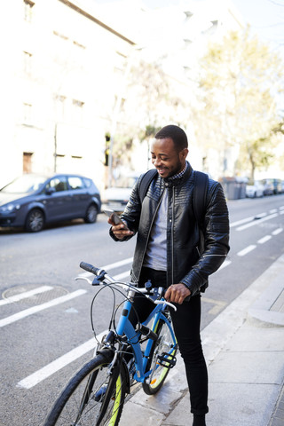 Lächelnder junger Mann mit Fahrrad, der sein Smartphone überprüft, lizenzfreies Stockfoto