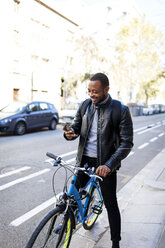 Lächelnder junger Mann mit Fahrrad, der sein Smartphone überprüft - VABF00961