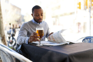 Junger Mann liest Zeitung und trinkt ein Bier in einem Straßencafé - VABF00962