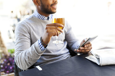 Junger Mann mit Smartphone trinkt ein Bier in einem Straßencafé - VABF00964