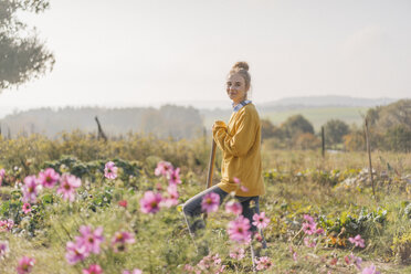Lächelnde junge Frau mit Spaten im Garten eines Landhauses - KNSF00752