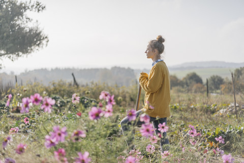 Junge Frau mit Spaten im Garten eines Hauses, lizenzfreies Stockfoto