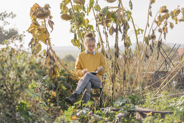 Junge Frau liest ein Buch im Garten eines Landhauses - KNSF00769