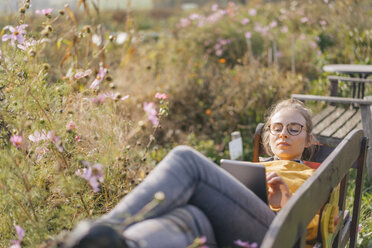 Young woman using tablet in cottage garden - KNSF00779