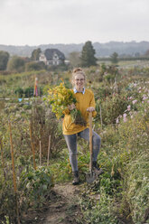 Lächelnde junge Frau, die eine Pflanze im Garten eines Landhauses hält - KNSF00784