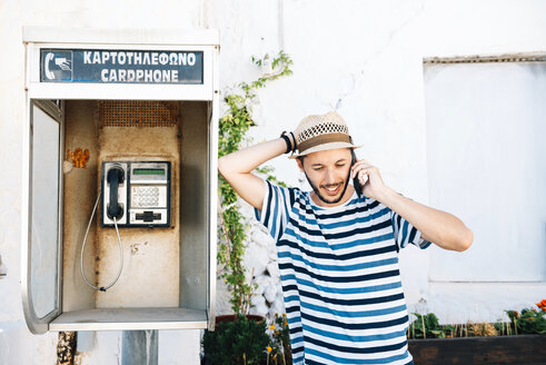 Griechenland, Milos, Klima, Mann spricht mit Handy, lehnt sich an alte Telefonzelle - GEMF01338
