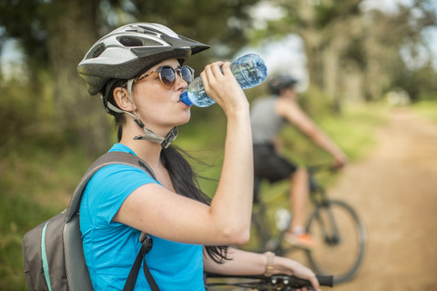 Junges Paar beim Mountainbiking in der Natur, Frau trinkt Wasser, lizenzfreies Stockfoto